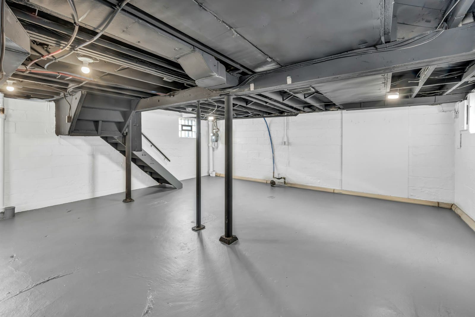 Clean unfinished basement with painted block walls, fresh grey floor and support posts