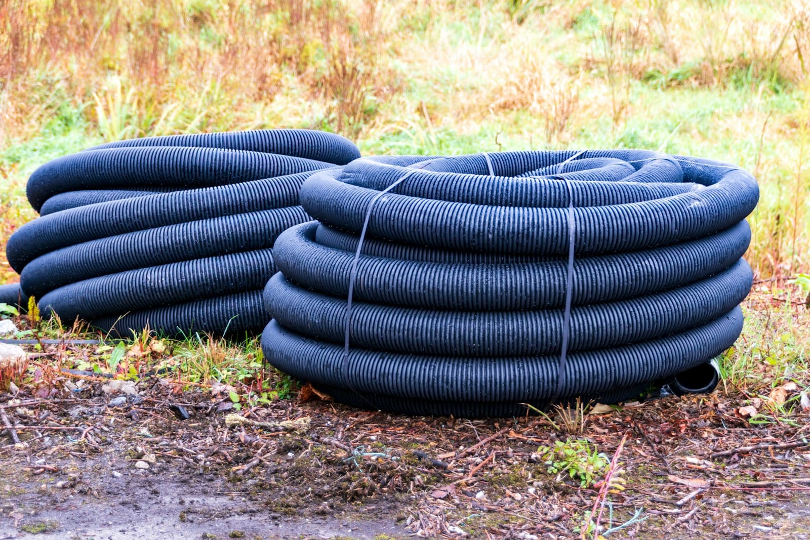 Coils of black perforated corrugated drainage pipe on a job site